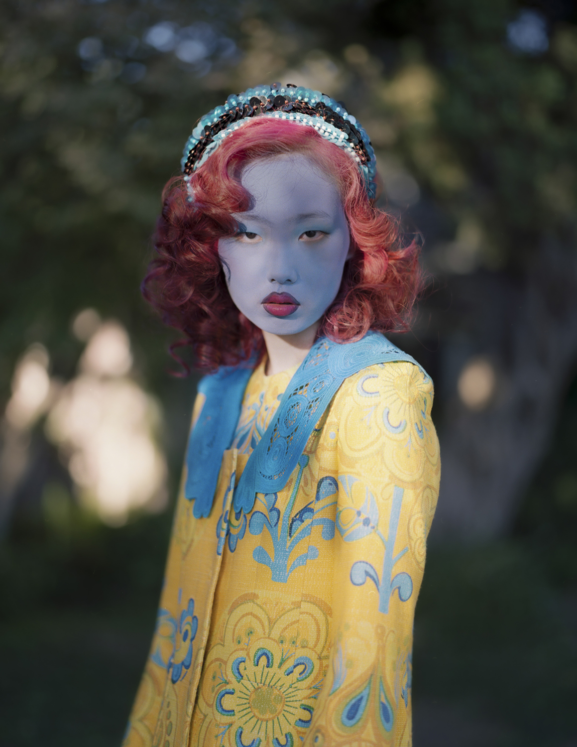 Full body shot of a model with blue facepaint and red lips outdoors in a garden setting